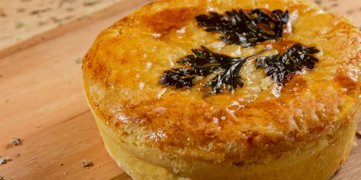 Tarte au thon dorée coupée en parts, tomates et moutarde visibles, sur une table en bois, style cuisine maison